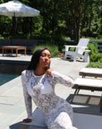 Woman in a white lace dress sitting by a poolside with greenery in the background