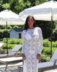 Woman in a white lace dress standing outdoors with lounge chairs and umbrellas in the background.